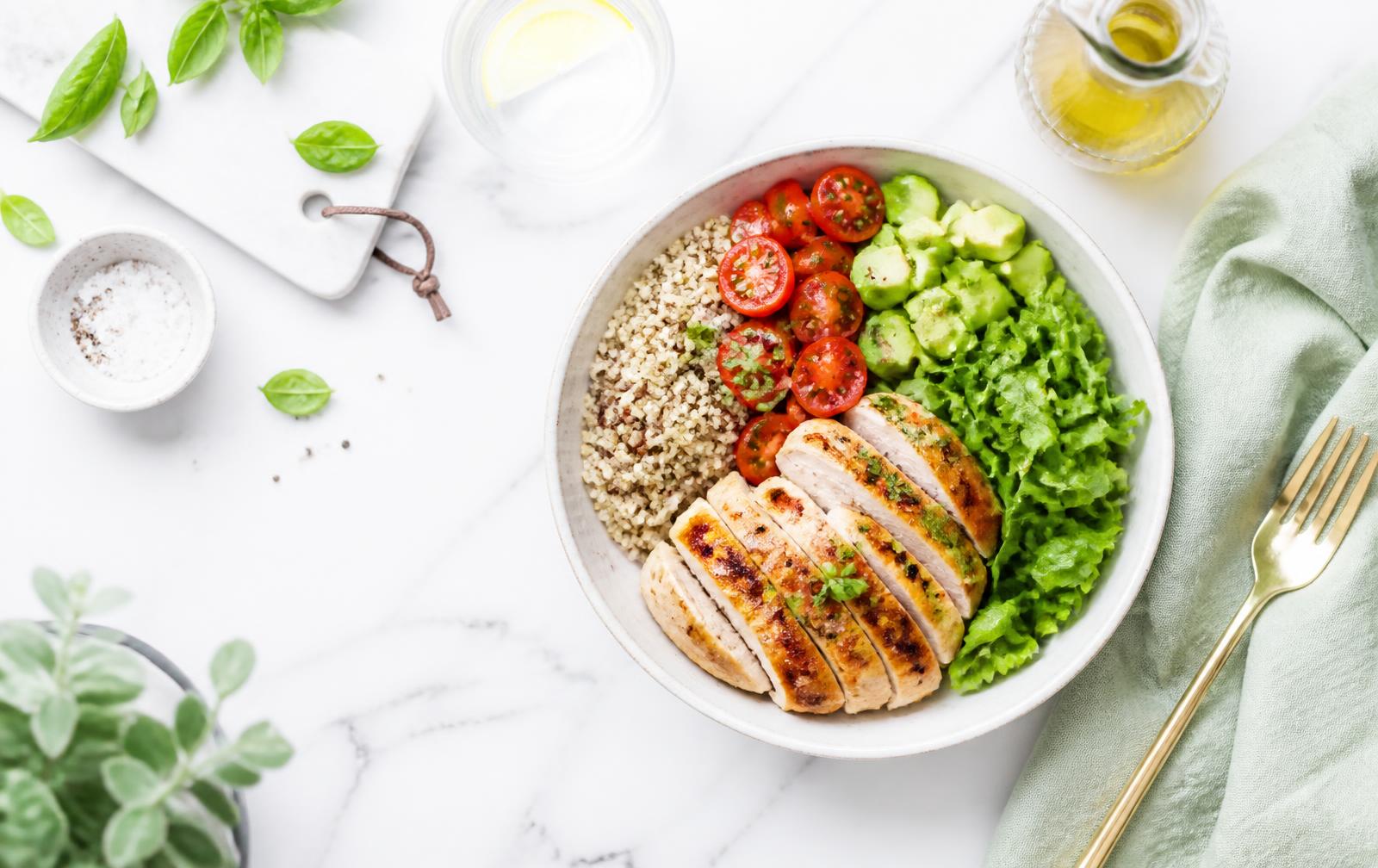 Bowl con pollo grigliato, quinoa, pomodorini e avocado su marmo bianco